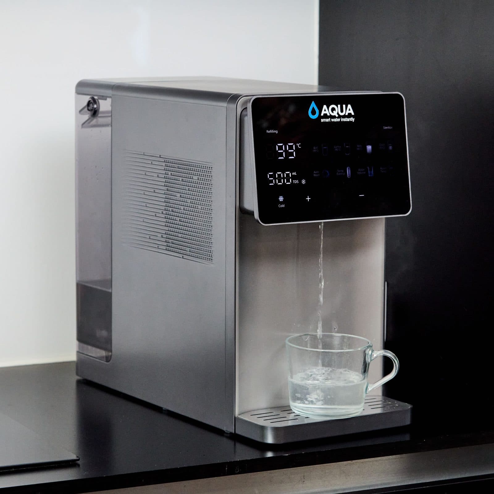 Aqua pouring hot water into a glass mug, display reading 99°